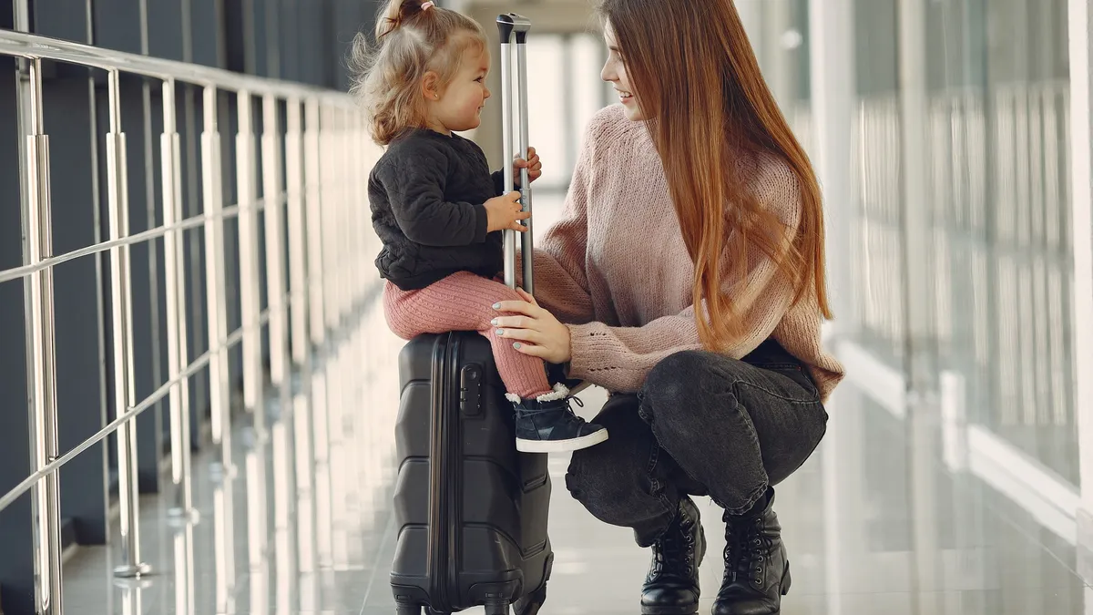 Mama ir dukra su lagaminu šiuolaikiniame oro uosto terminale.