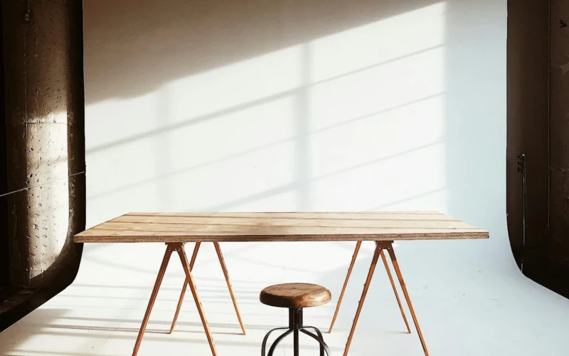 A wooden table on trestle legs and a stool in a sunlit studio